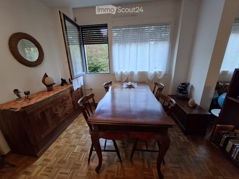 Dining room with a long wooden dining table surrounded by chairs, a wooden cabinet with decorative items, and a round mirror on the wall.