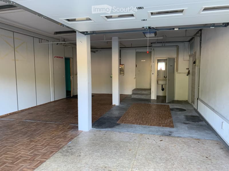Empty garage with concrete floor, wooden flooring in one section, white walls, and a small wash area with a sink and steps.
