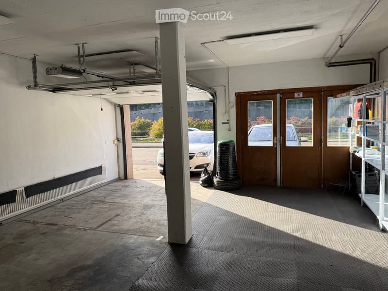 Empty garage with concrete floor, metal shelving, and a partially open door revealing a parked car outside.
