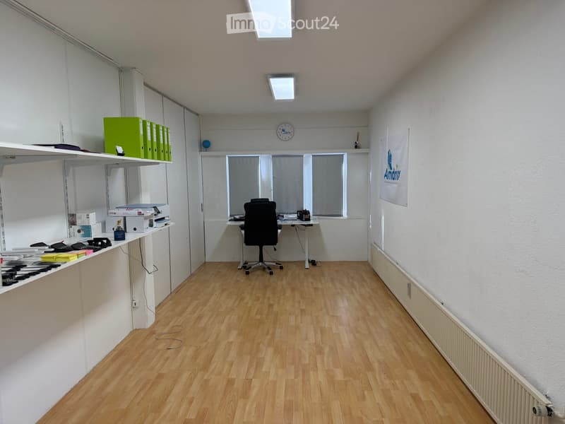 Office space with wooden flooring, a desk with a chair, shelves holding binders and office supplies, and a banner on the wall.