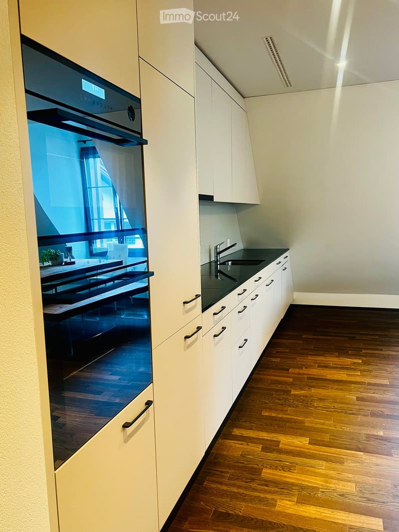 Modern kitchen with white cabinets, dark countertops, and a built-in oven. Wooden flooring and sleek design.
