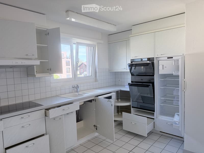 Modern kitchen with white cabinets, a sink, an oven, and a refrigerator. The cabinets are open, revealing empty shelves.