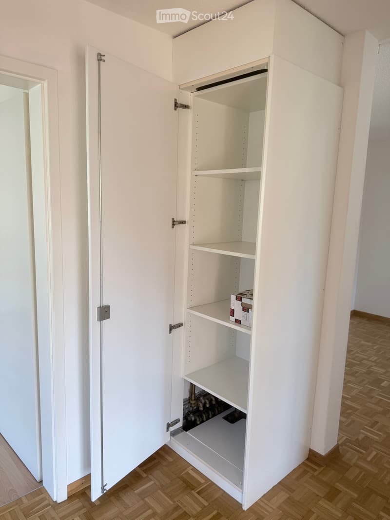 An empty room with a built-in white cabinet featuring multiple shelves and a lower compartment, with a wooden floor and white walls.