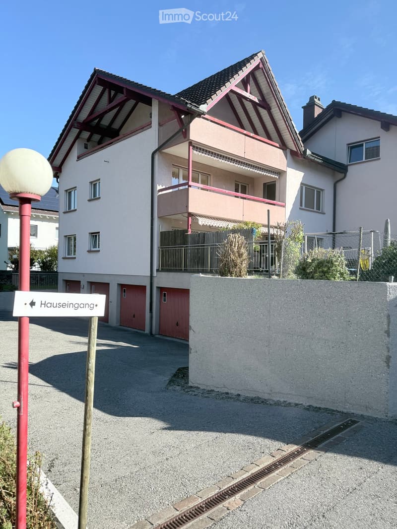 Two-story house with a balcony, red garage doors, and a sign pointing to the house entrance.