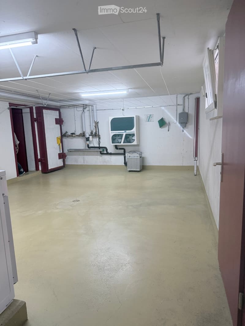 Empty utility room with concrete floor, white walls, exposed pipes, and a small air conditioning unit.