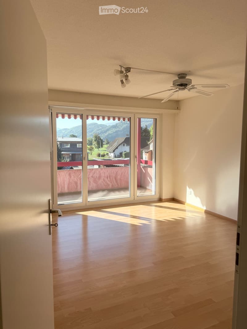 Empty room with wooden flooring, large sliding glass doors leading to a balcony with a scenic mountain view.