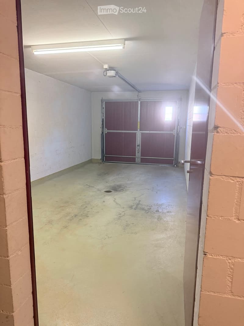 Empty concrete corridor with white brick walls, fluorescent lighting, and a large metal gate at the end.