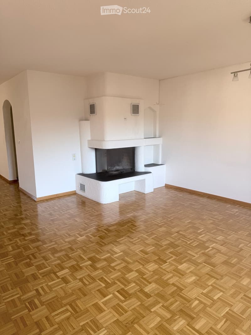 Empty room with wooden herringbone flooring and a white fireplace with black insert. Light-colored walls and ceiling.