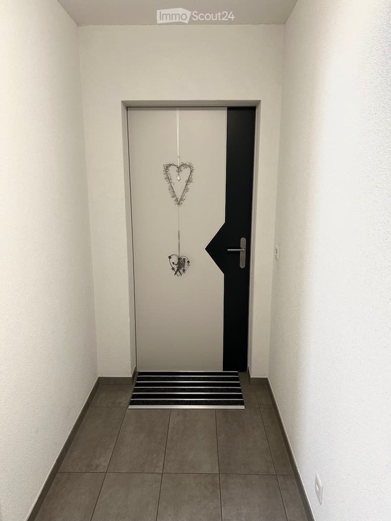 A narrow hallway with white walls, tiled floor, and a door with decorative heart-shaped ornaments.