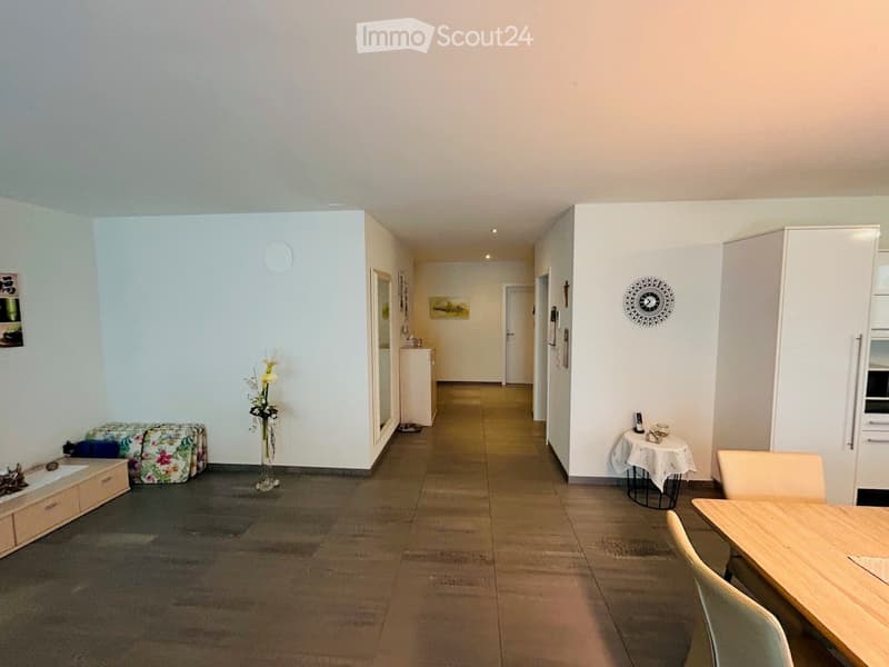 A clean, well-lit hallway with tiled flooring, white walls, and several doors leading to different rooms. There are small decorative items and furniture visible along the walls.