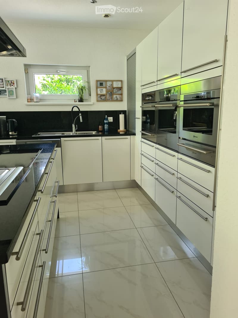 Modern kitchen with white cabinets, stainless steel appliances, marble flooring, and a black countertop.