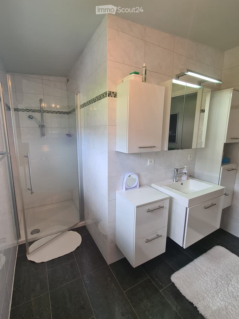 Modern bathroom with white tiles, a glass-enclosed shower, two sinks, a mirror, and white cabinets.
