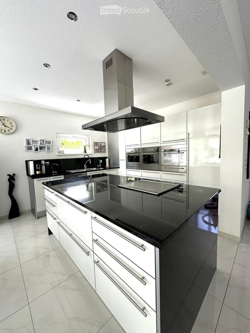 Modern kitchen with white cabinets, black countertops, stainless steel appliances, and a central island.
