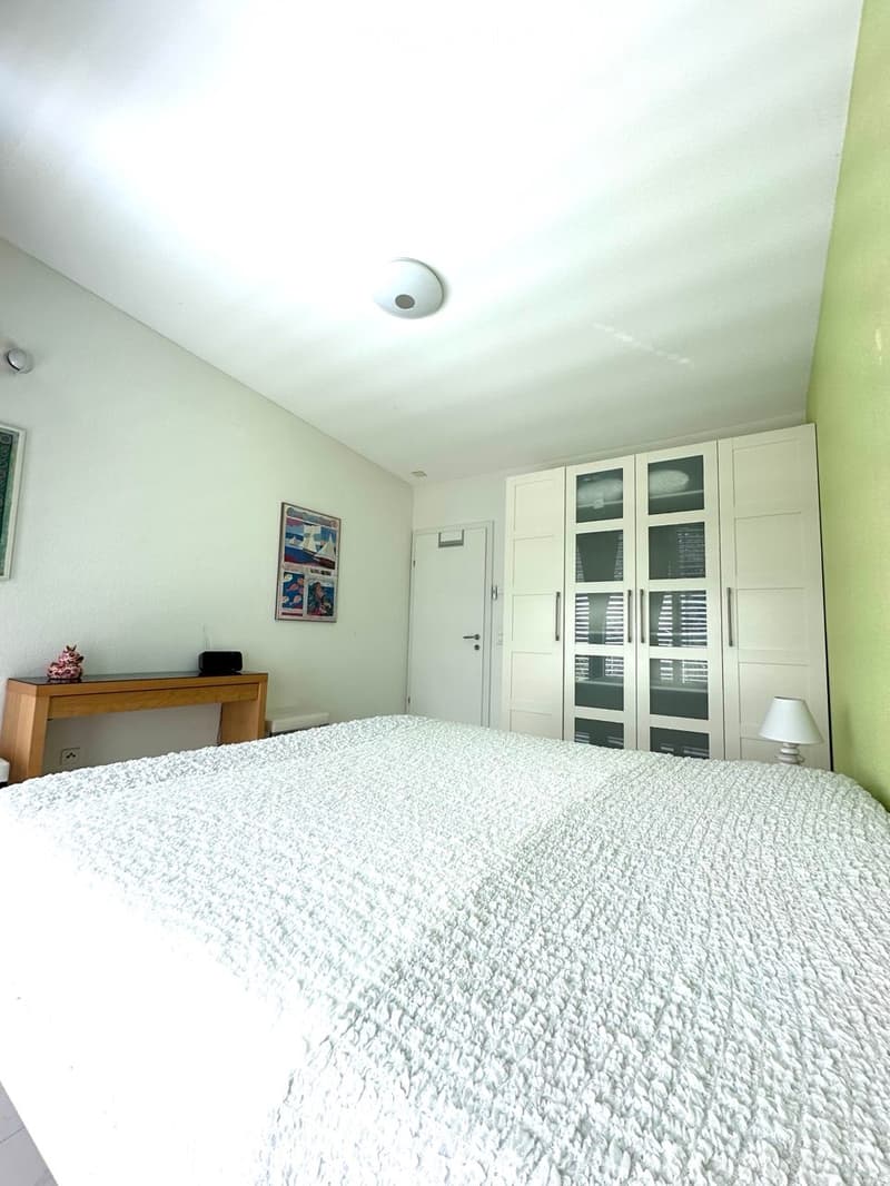 A modern bedroom with a large bed, white wardrobe, small wooden table, and a lamp on the side.