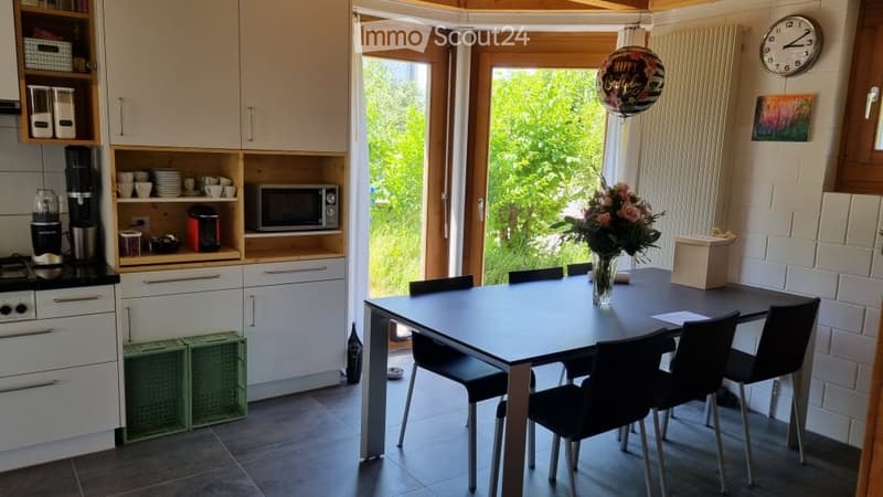 Bright, modern kitchen and dining area with white cabinets, a black dining table with six chairs, a vase of flowers, and a microwave on the counter.