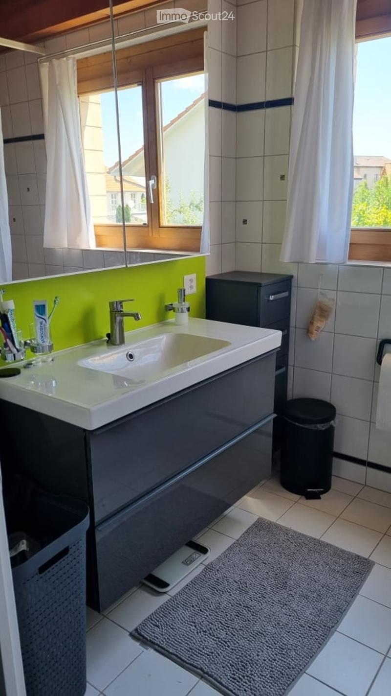 Modern bathroom with a white sink, grey cabinet, mirror, and a bright green accent wall. Includes a toothbrush holder, toothpaste, and a small trash bin.
