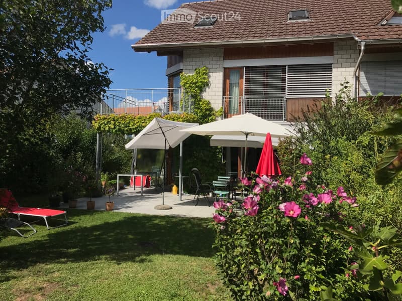 Garden with a patio area, outdoor furniture, and a house with a balcony in the background.