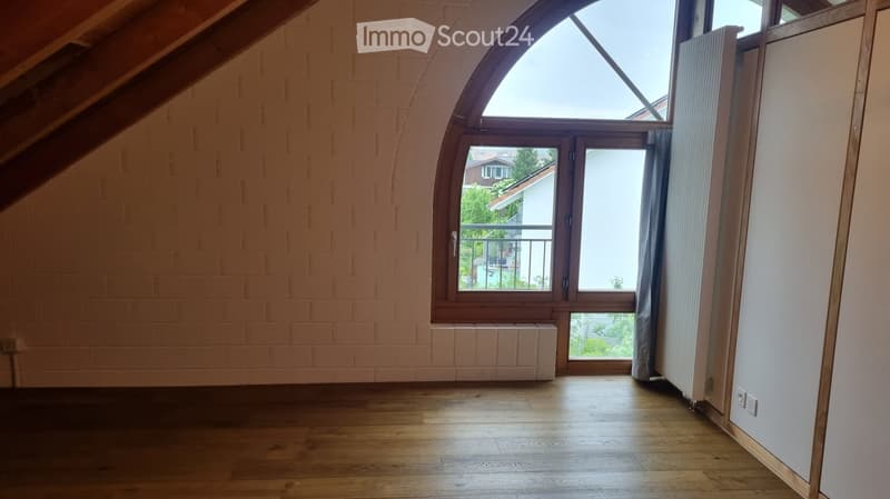 Empty room with wooden flooring, exposed brick walls, large arched window, and radiator. No furniture or equipment present.