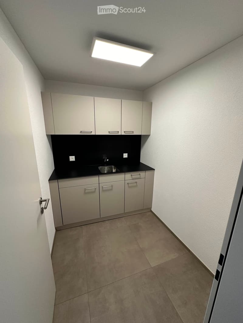 Empty kitchen area with light-colored cabinets, a sink, and a tiled floor.