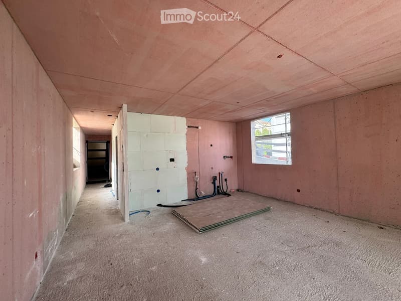 Empty room with unfinished walls and floor, visible electrical wiring and a window with bars.