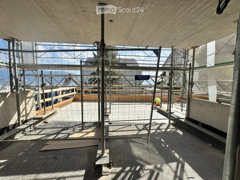 Empty construction site with exposed concrete floor, metal scaffolding, and wooden planks. No furniture or equipment present.