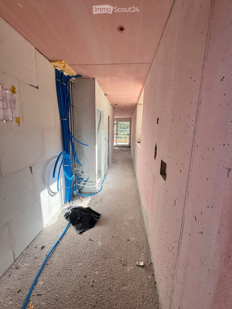 Empty hallway with unfinished walls, exposed wiring, and a black bag on the floor.