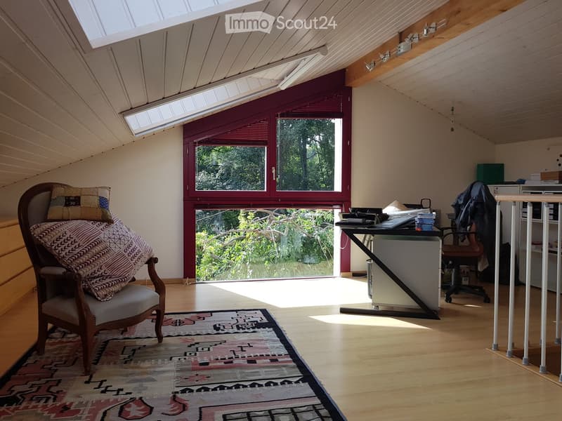Attic with large window, wooden desk, chair, carpet, and cabinet