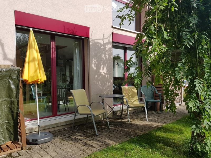 Outdoor area with brick ground, table, chairs, yellow umbrella, garden, glass door, plants
