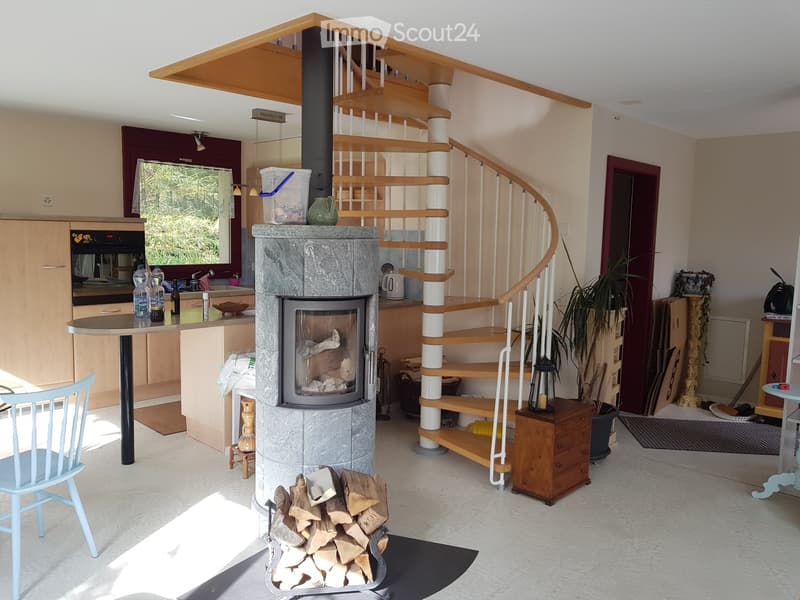 Wood-burning fireplace, kitchen with appliances, open staircase, white floor, wooden staircase, small round table with chairs, open room layout