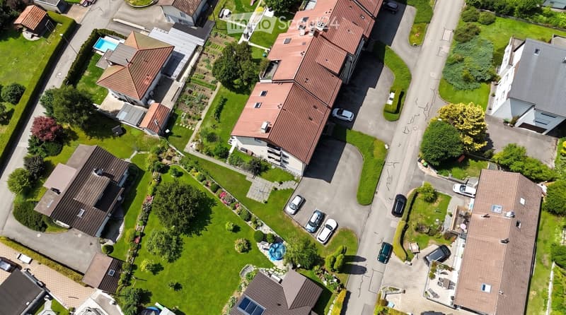 Aerial view of a residential neighborhood with multiple houses, well-maintained lawns, driveways, and a swimming pool visible in one of the yards.