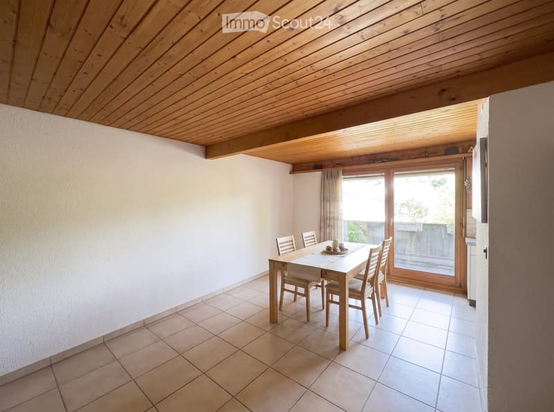 Dining room with a wooden dining table and chairs, tiled floor, large window with a view, and a wooden ceiling.