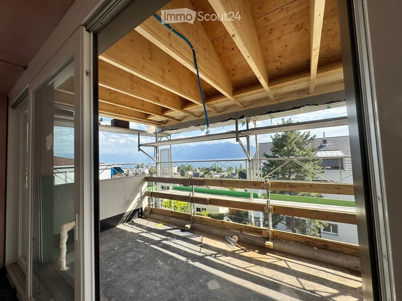Balcony with wooden beams, metal railing, and a view of a cityscape and mountains.