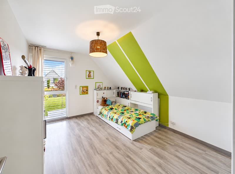 Bright, modern bedroom with a built-in bed and wardrobe, colorful bedding, pendant light, and picture frames on the wall. The room features wooden flooring and a large window with a view of the garden.