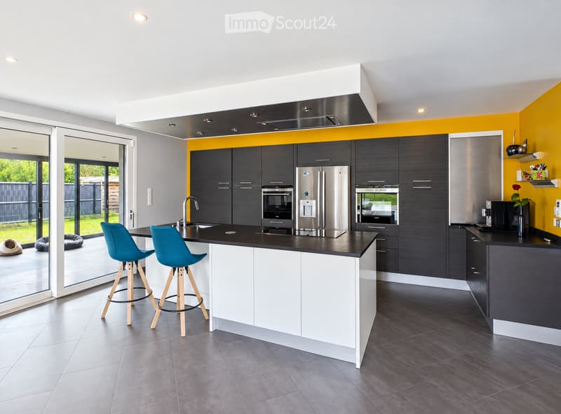 Modern kitchen with dark grey cabinets, white island, black countertops, stainless steel appliances, and two blue stools.