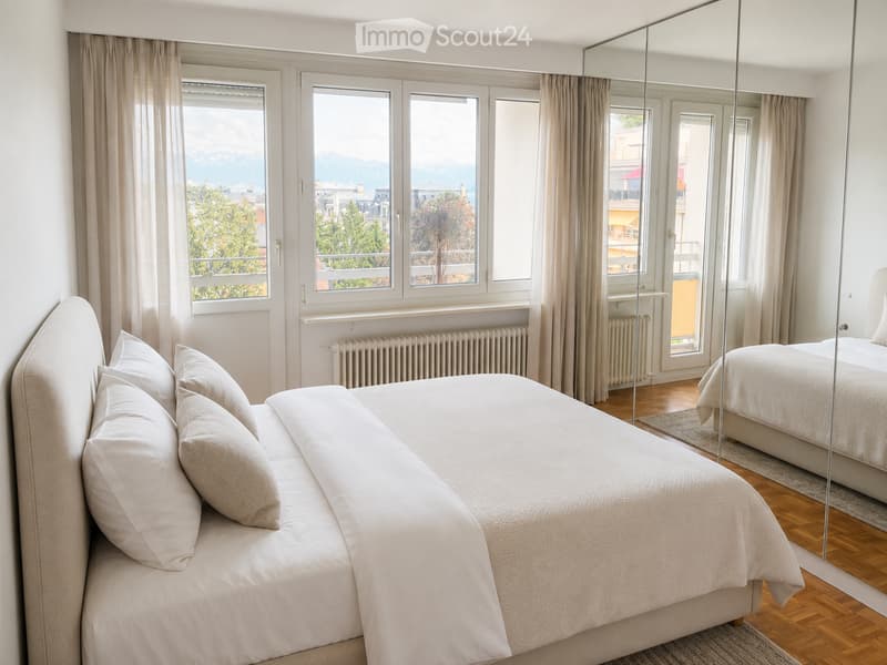 Elegant bedroom with a large bed, multiple pillows, a full-length mirror, and large windows offering a scenic view of the city and mountains.