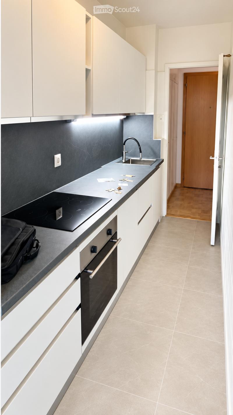 Modern kitchen with white cabinets, a black countertop, an induction stove, an oven, and a sink with a modern faucet. The floor is tiled, and a wooden door leads to another room.
