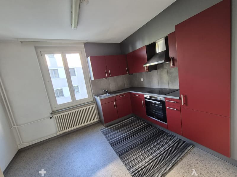 Modern kitchen with red cabinets, stainless steel appliances, and a large window providing natural light.