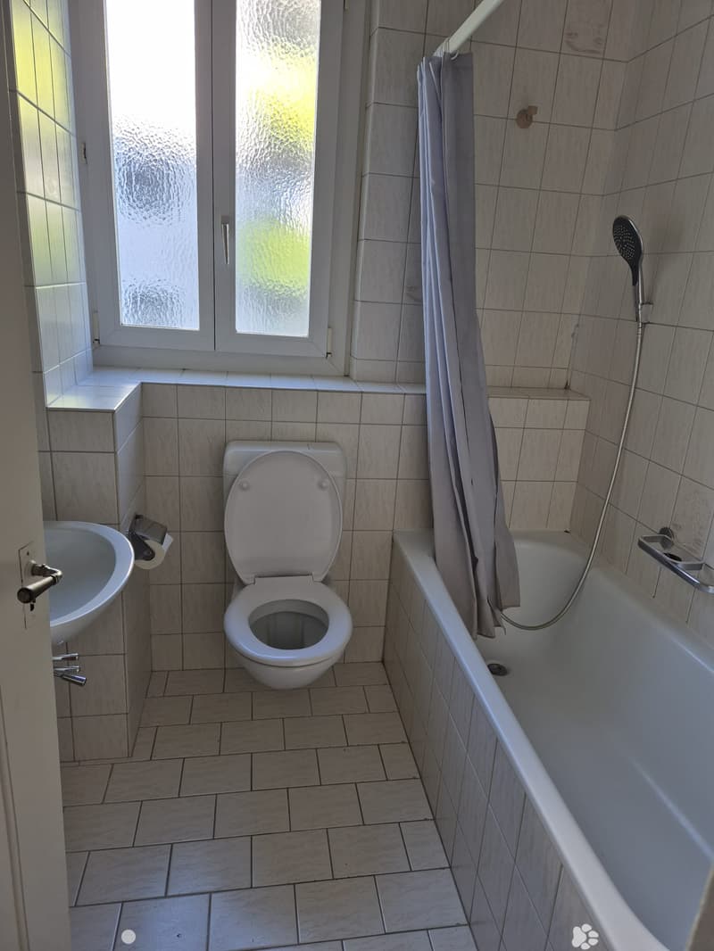 Bathroom with tiled walls and floor, featuring a toilet, bathtub with a shower curtain, and a sink.