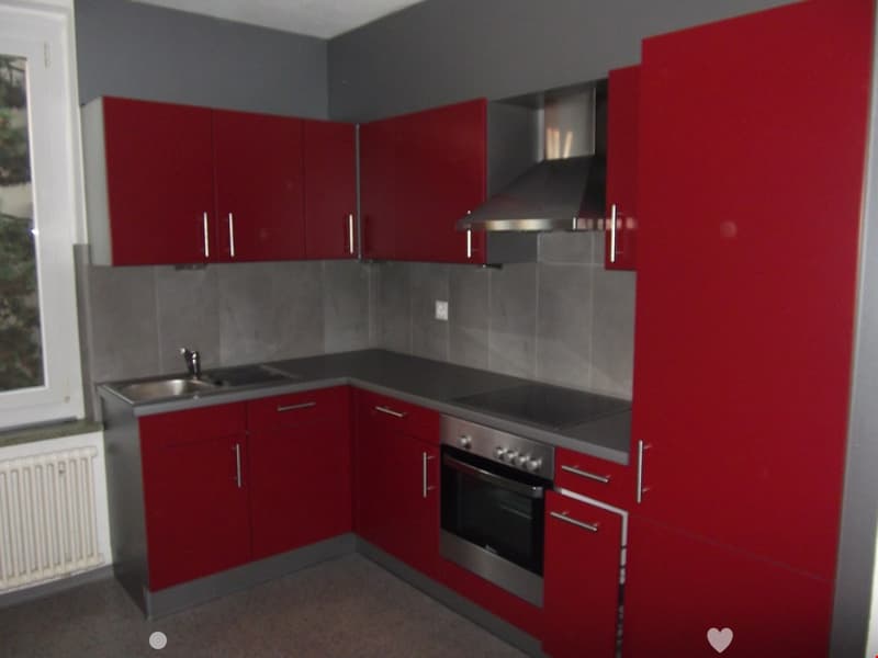 Modern kitchen with red cabinets, stainless steel appliances, and a grey tiled backsplash.
