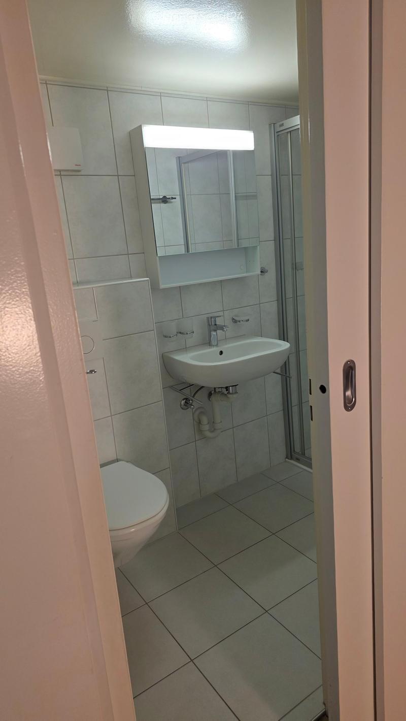Modern bathroom with a toilet, sink, and mirror. The walls are tiled, and the floor is covered with square tiles.