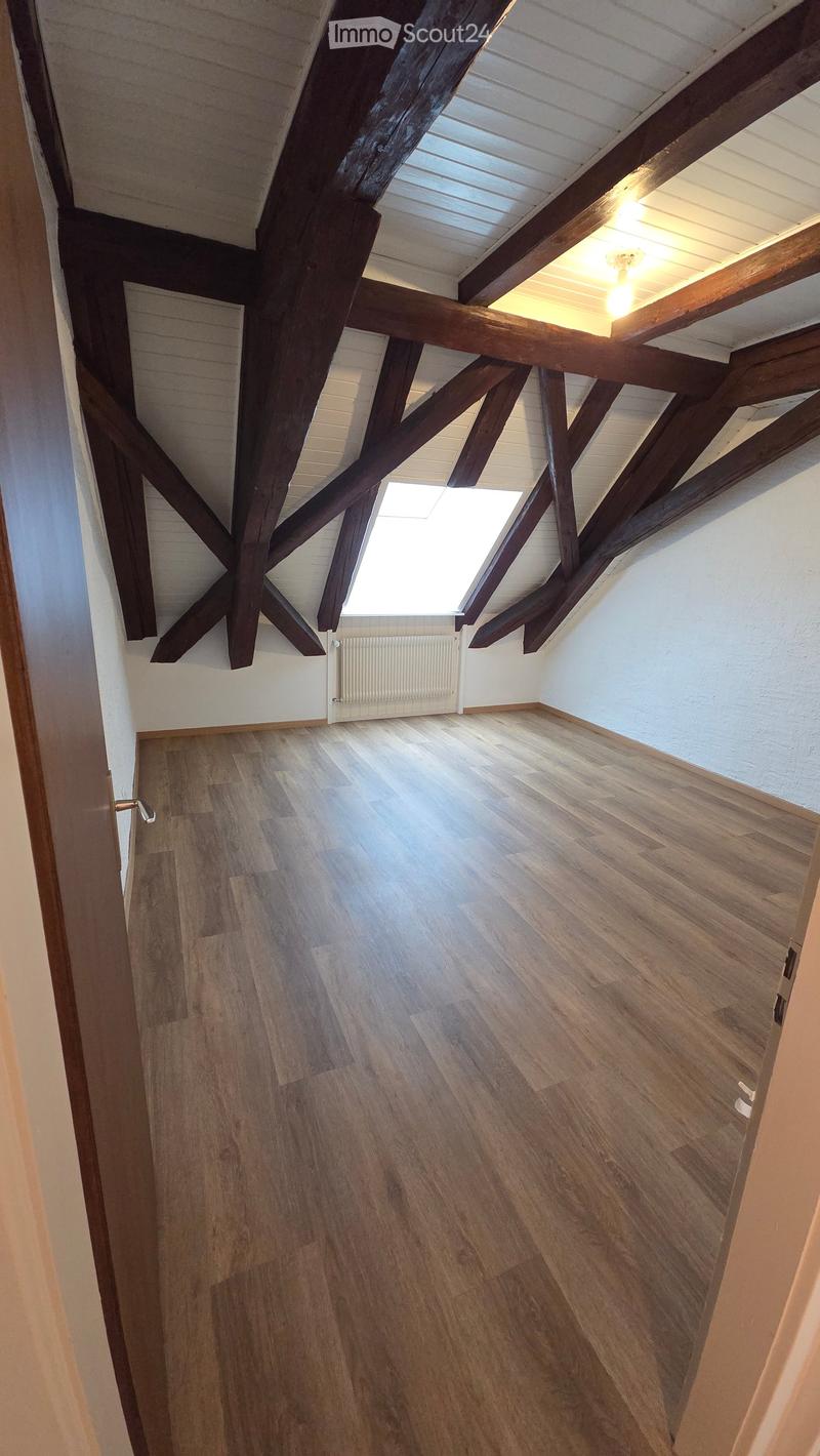 Empty attic space with wooden beams, wooden flooring, and a skylight window. No furniture or equipment present.