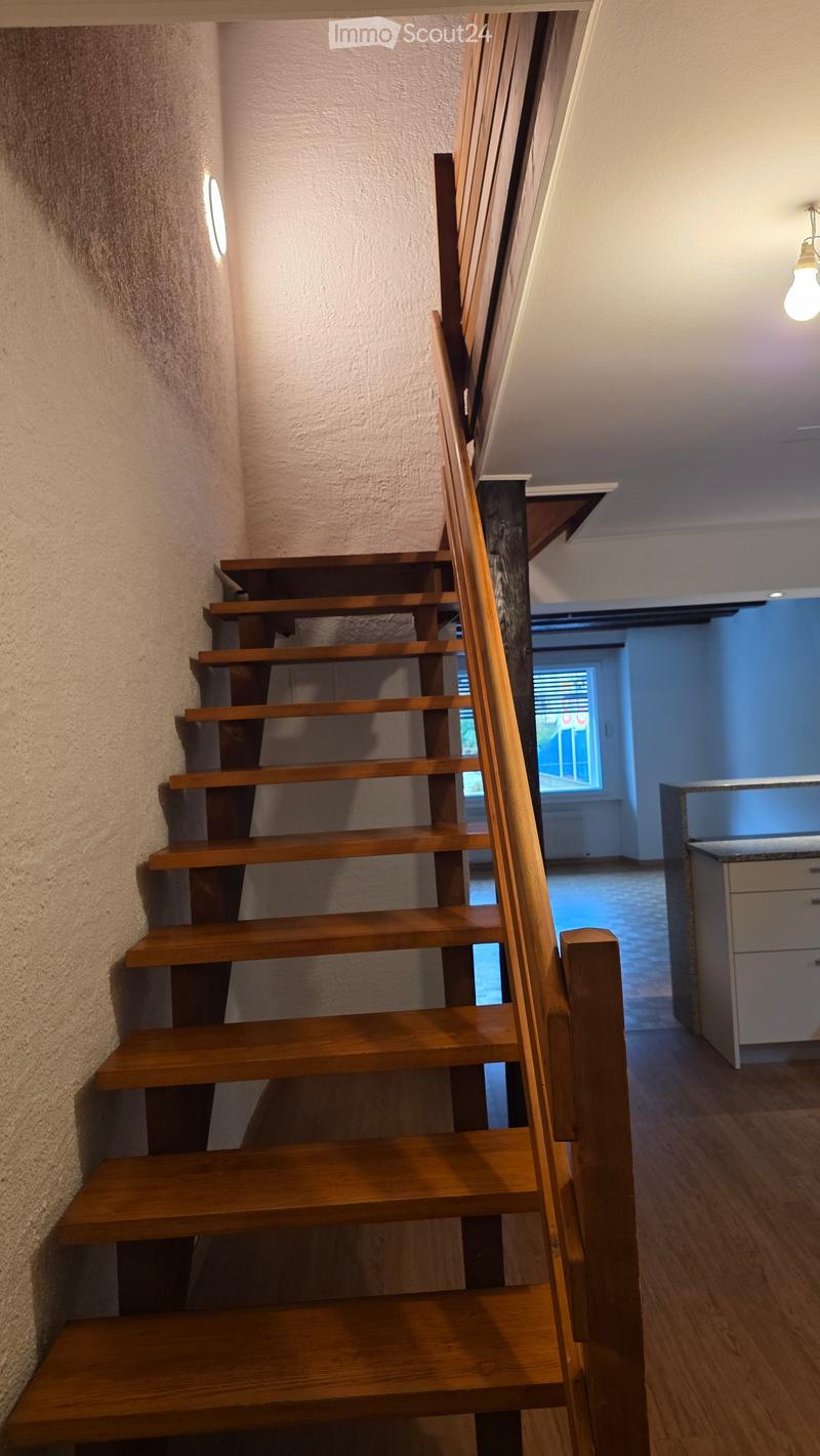 Wooden staircase with modern railing, soft lighting, and a view into a room with a window and cabinetry.