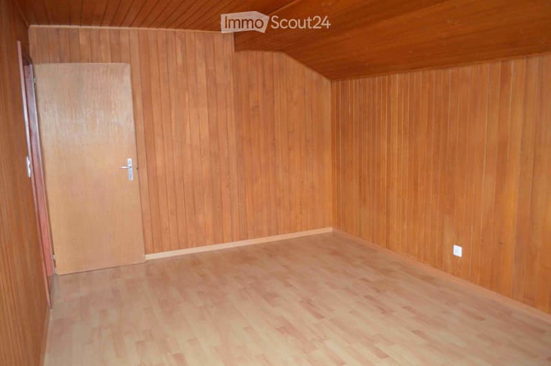 Empty room with wooden walls and flooring, featuring a single door and a visible electrical outlet.