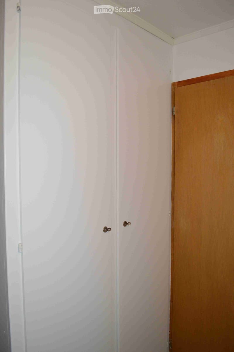 Empty room with light-colored walls and a wooden door, featuring a simple interior with no furniture or decorations.