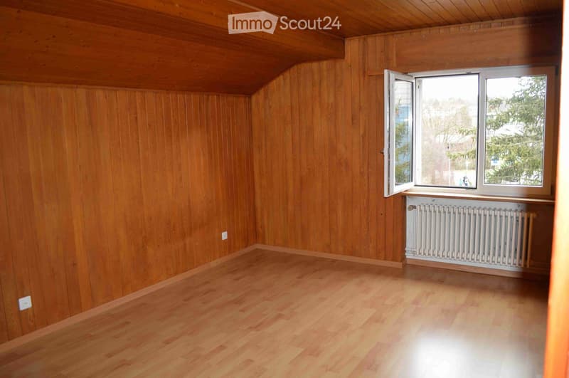Empty room with wooden walls and floor, large window with open shutters, radiator below window, and visible electrical outlets.