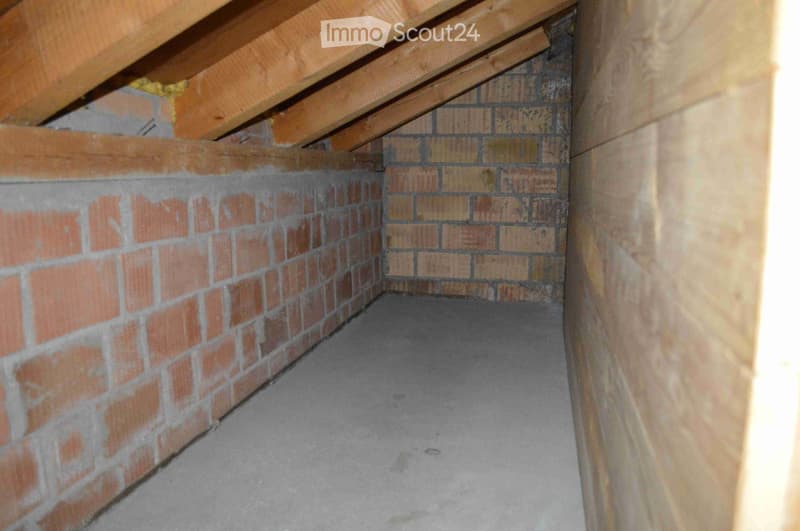 Empty attic space with exposed wooden beams, brick walls, and a concrete floor.