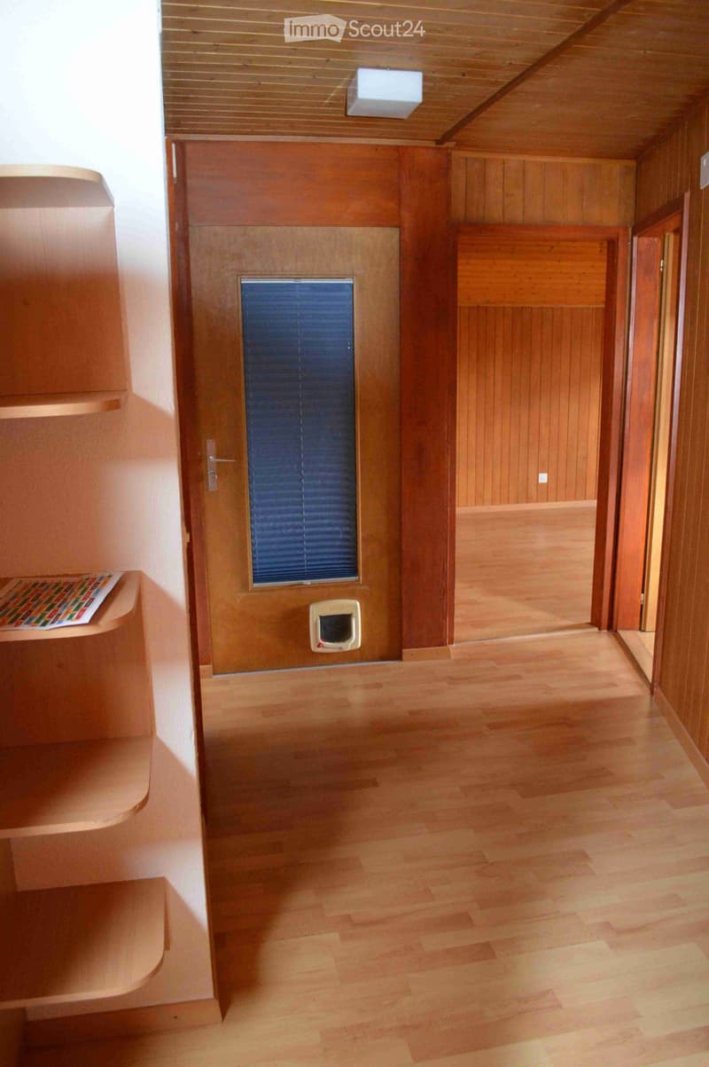Wooden hallway with light-colored flooring, wooden walls, and a small window with blinds. A pet door is visible on the wall.