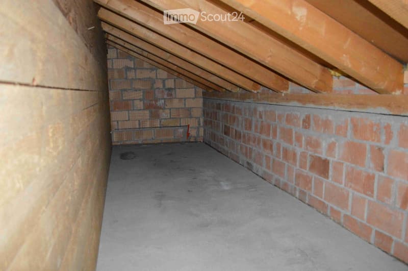 Empty attic space with exposed wooden beams, brick walls, and concrete floor. No furniture or equipment present.