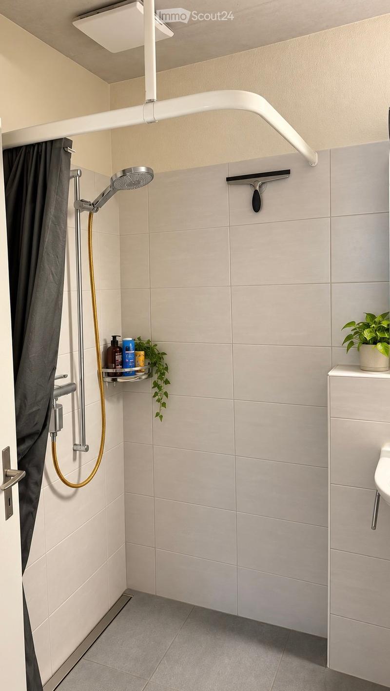 Modern bathroom with a walk-in shower area, featuring a sleek showerhead, a dark shower curtain, a built-in shelf holding toiletries and a small plant, and a white toilet with a modern faucet.