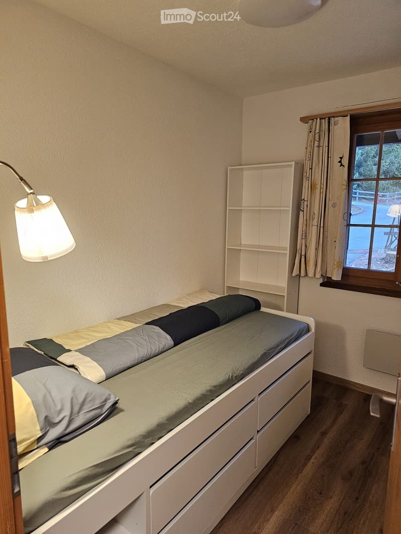 Cozy bedroom with a single bed, built-in storage drawers, a small shelf, and a window with curtains.
